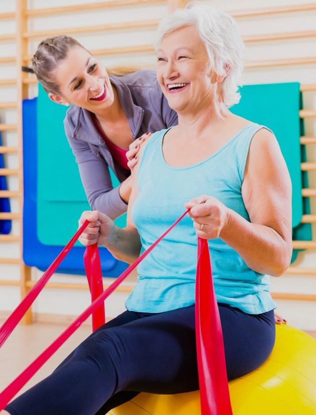 A woman is sitting on an exercise ball with an older woman.
