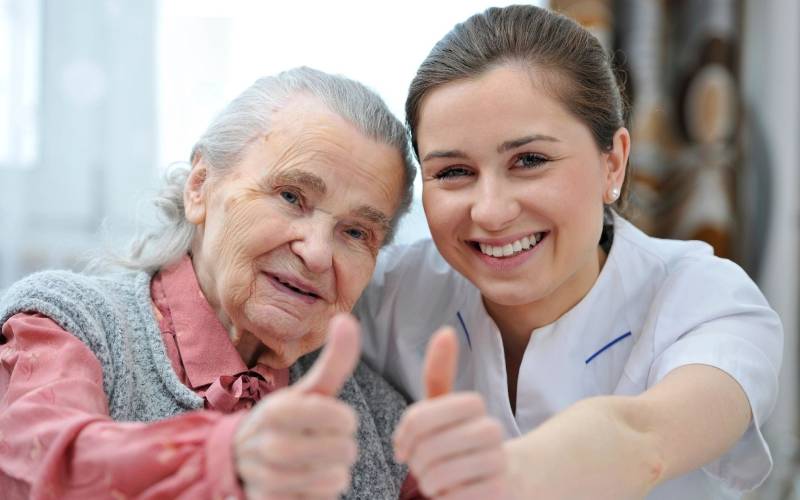 A nurse giving a thumbs up to an elderly woman.