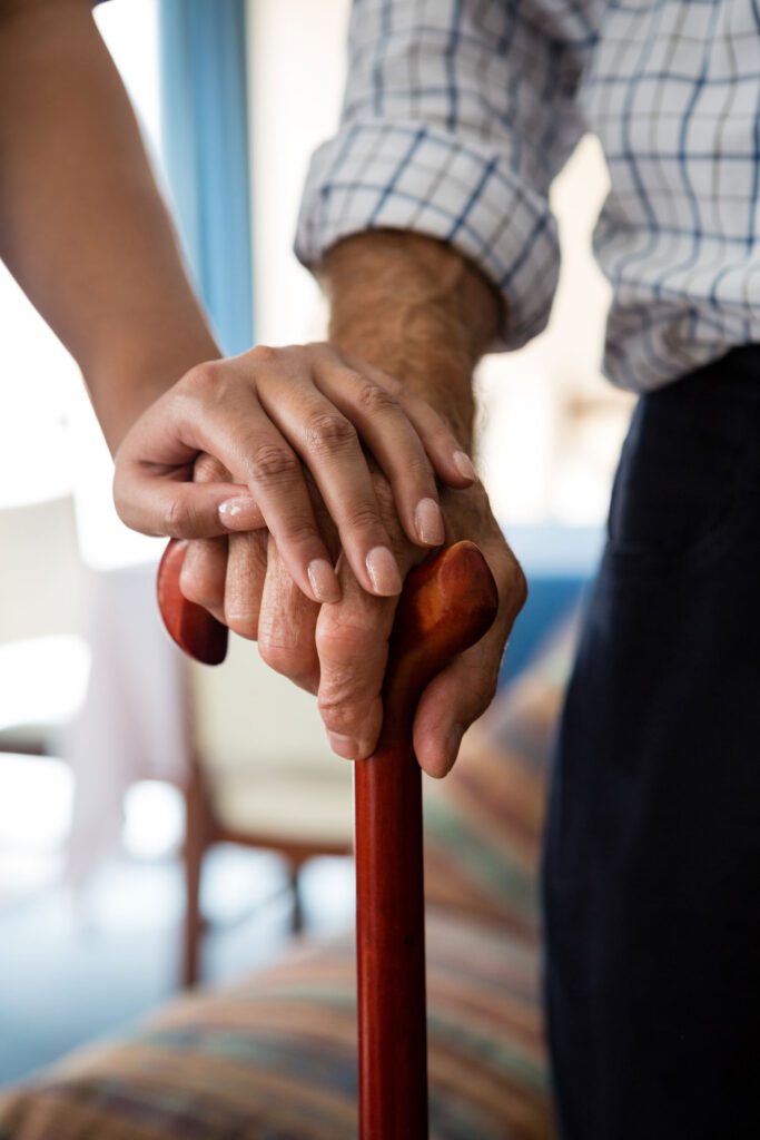 A man holding an elderly woman's hand with a cane.