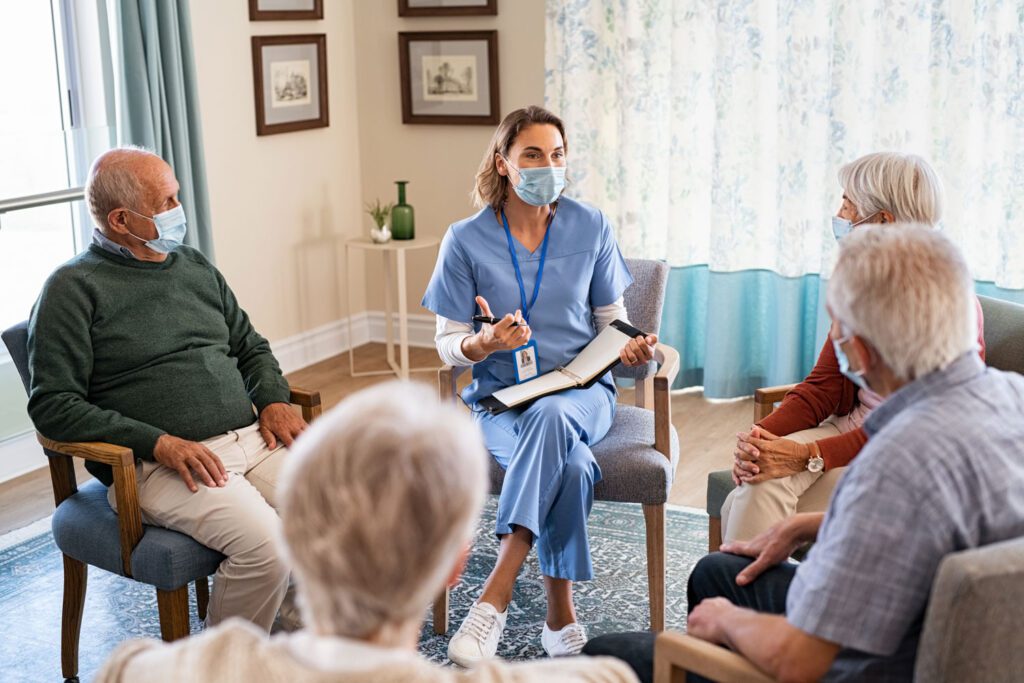 A group of elderly people sitting in a room with a nurse in a mask.