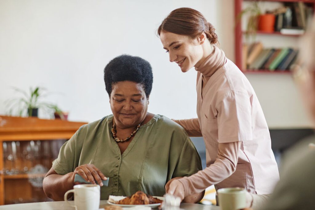 A nurse is helping an elderly woman eat breakfast.