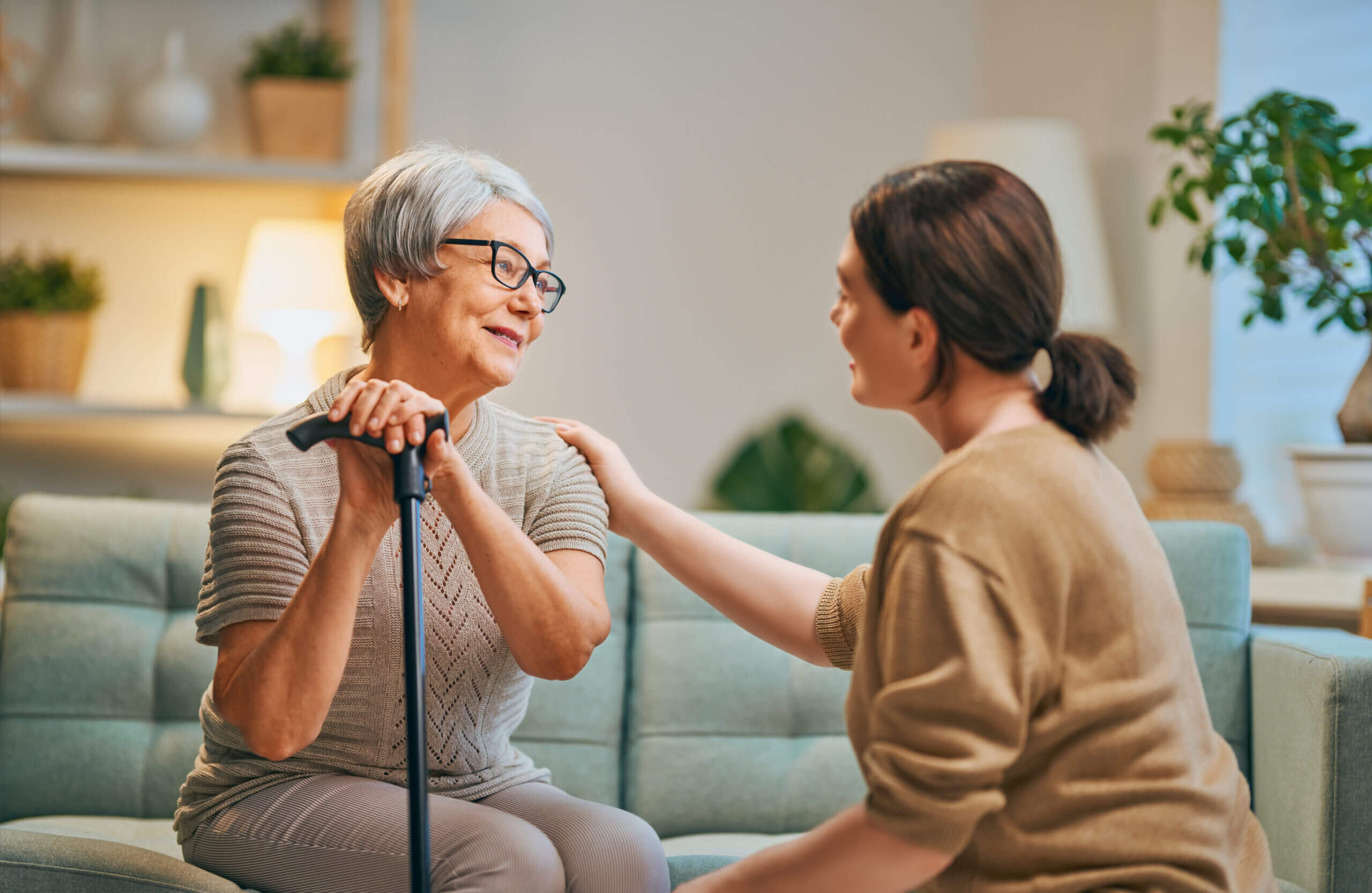 A woman is helping an elderly woman with a cane.